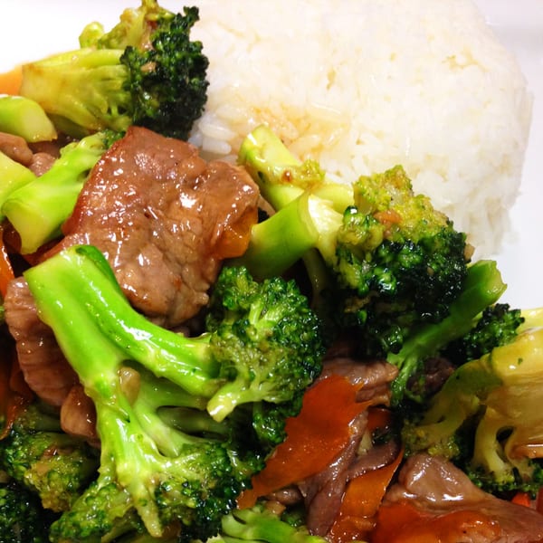 Thai beef and broccoli stir-fry with carrots and white rice on a white plate.