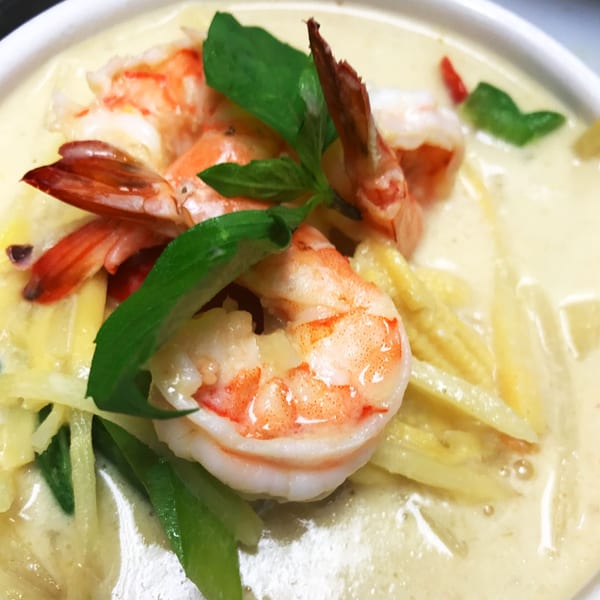 Close-up of Thai green curry with shrimp, bamboo shoots, and basil in a white bowl.